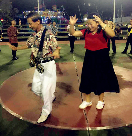 黄文能(左1)在农场职工文化广场教采风团记者跳舞。(耿洁 摄)