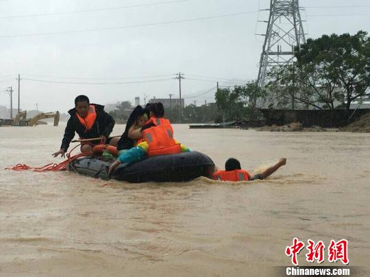 消防官兵利用橡皮艇救助受灾民众，由于水中无法前行，官兵跳入水中拉着皮筏前进。消防供图