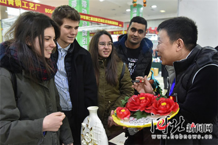 一位陶瓷商正向几名来自石家庄四十二中的外国留学生介绍中国传统节日饰品牡丹瓷。