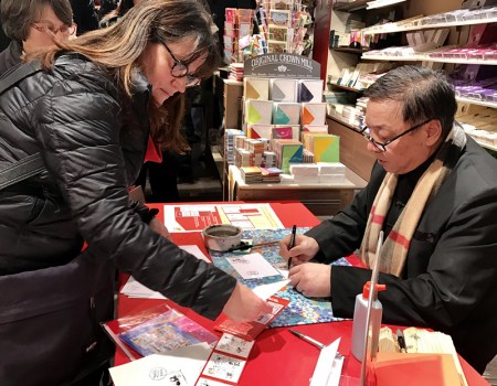 邮票设计者、华裔艺术家李中耀为法国集邮爱好者签名。(法国《欧洲时报》/张新 摄)