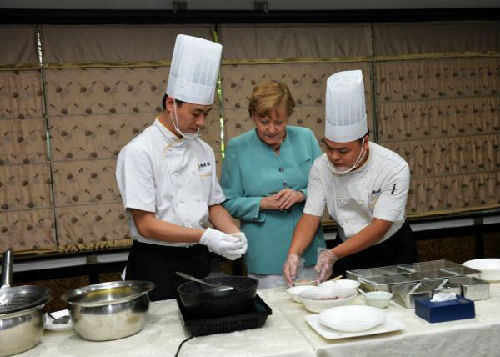 2014年7月6日，德国总理默克尔(中)在成都一家餐厅学习川菜宫保鸡丁的做法。新华社发