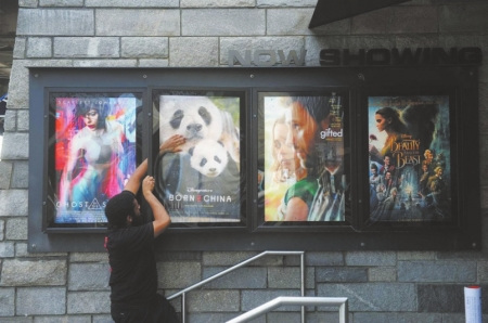AMC影院的工作人员费莱迪将影片《我们诞生在中国》电影海报挂在展示栏中。