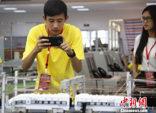 一名华裔青少年用手机拍摄高铁运行沙盘。　朱柳融 摄