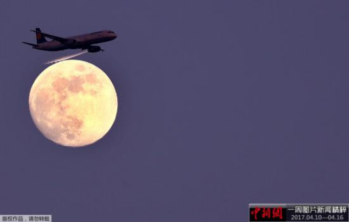 资料图：一架客机从月亮前飞过。