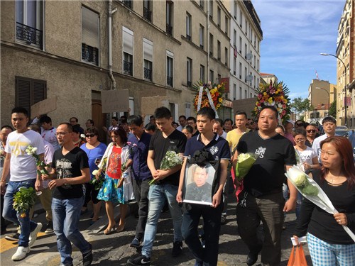 张朝林之子捧着父亲遗像与华人同胞一起上街请愿。（法国《欧洲时报》/黄冠杰 摄）