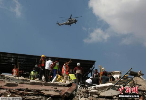 目前，墨西哥政府已出动军队参与救灾、维持灾区秩序。在墨西哥城，有志愿者和救援人员在废墟中寻找幸存者。图为一架军用直升机从建筑废墟上飞过。