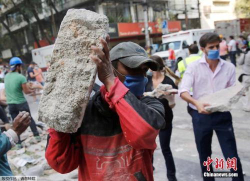 墨西哥城的一处倒塌的建筑废墟旁，志愿者徒手搬走石块，以方便救援行动展开。