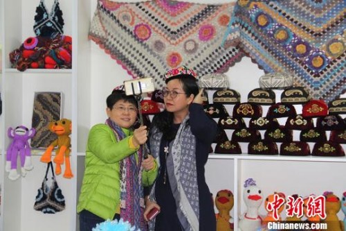 图为海外华文媒体高层代表在第十二师头屯河农场同和幸福社区戴着女职工编织的小花帽拍照。　袁晶 摄