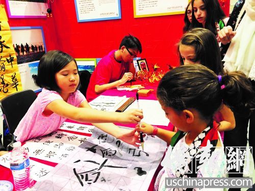 小朋友李博淼(左)教小客人握毛笔。（美国《侨报》/毛苌子 摄）