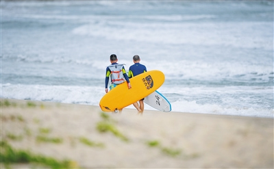 日月湾，游客拿着冲浪板去冲浪。
