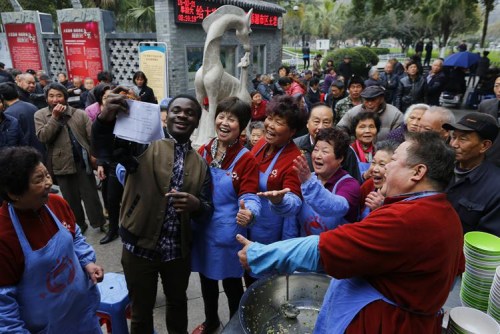 图7:2015年农历二月初二,当日来红日亭吃芥菜饭的路人很多,温州医学院留学生艾鹏达闻讯后来红日亭当义工。在场的红日亭老人们纷纷与艾鹏达开心留影。 图7:2015年农历二月初二,当日来红日亭吃芥菜饭的路人很多,温州医学院留学生艾鹏达闻讯后来红日亭当义工。在场的红日亭老人们纷纷与艾鹏达开心留影。