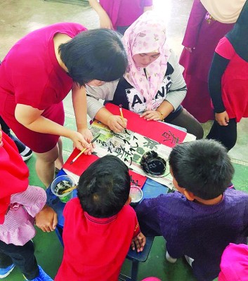 诚育学校的教师教导友族家长如何写书法。(马来西亚《光华日报》)