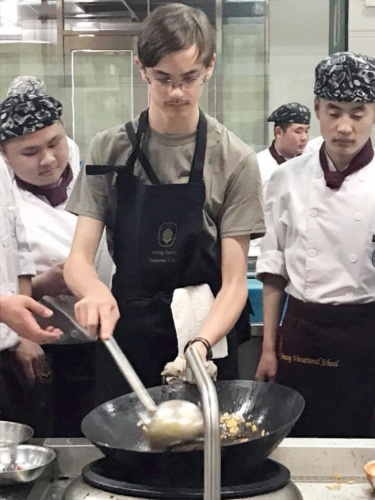 戴维(中)学习炒宫保鸡丁。(美国《世界日报》/东点学校供图)