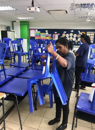 校工正在清洗桌椅及进行消毒工作。（马来西亚《星洲日报》）