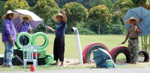 大家戴着草帽、撑着伞，在烈日下美化校园。（马来西亚《星洲日报》）