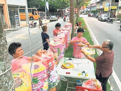 村民分工合作将透明的塑料袋倒套着纸制的灯笼，避免灯笼被雨淋湿或被曝晒损坏。（马来西亚《中国报》/村民提供照片）