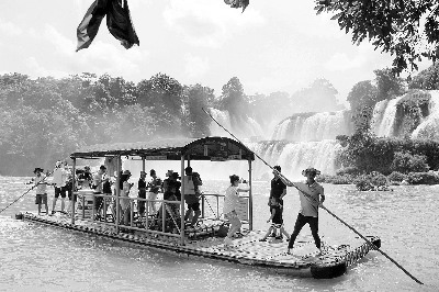 图：游客在中越边境的归春河上观赏瀑布（郭凯倩）