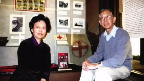 　在胡佛研究院的二战文物展上，张纯如的父母张绍进、张盈盈在他们女儿撰写的《南京大屠杀》和她捐献给研究院的、抗战期间拯救无辜百姓生命的红十字旗前留影。(美国《侨报》／陆杰夫摄)