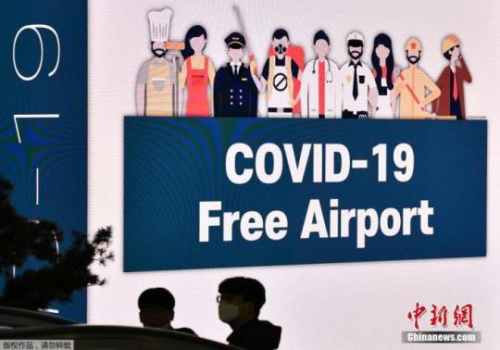 资料图：位于韩国首尔的仁川国际机场，戴着口罩的人们走过大屏幕。