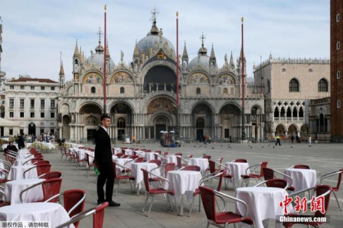 资料图：侍应生站在威尼斯圣马克广场一家餐馆外的空桌子旁。