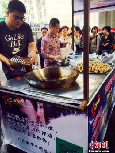 郭方正(左)正在往锅里倒炸鸡用的油,摊位边等待的顾客已排起长队。 曹铮 摄 郭方正(左)正在往锅里倒炸鸡用的油,摊位边等待的顾客已排起长队。 曹铮 摄