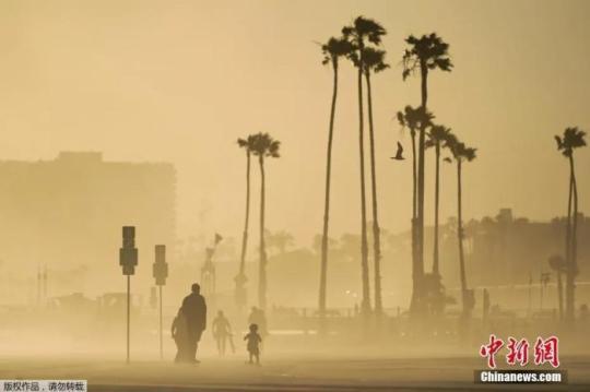 当地时间4月18日，美国加州海边大风卷起沙土，游客在漫天黄沙中出行。