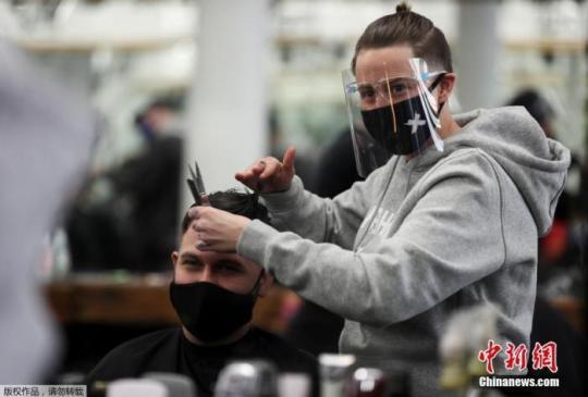 当地时间4月12日，英国纽卡斯尔一家理发店内，一名员工正在为顾客服务。