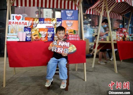 集市中，一名孩童手持“来柳州我粉你”的特色螺蛳粉语言留影。　蒙鸣明 摄