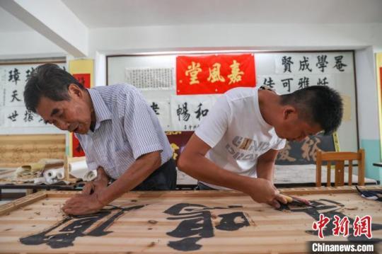 图为赣南客家匾额习俗的传承人肖天长(左)与自己的徒弟肖伟明(右)共同制作匾额。　刘力鑫 摄