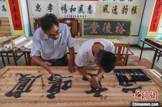 图为赣南客家匾额习俗的传承人肖天长(左)在指导自己的徒弟肖伟明(右)制作匾额。　刘力鑫 摄
