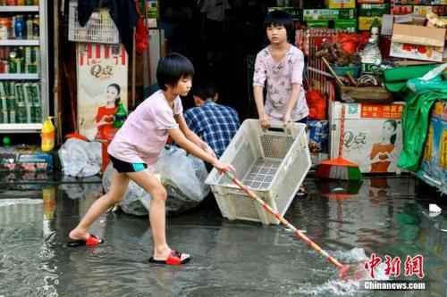 中国侨网资料图:9月3日,广东汕头市瓦窑村,两名女孩协助家长清理商铺外的积水。当日,广东汕头市潮南区天气转好,内涝地区积水水位逐渐下降。中新社记者 陈骥旻 摄