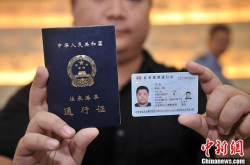 中国侨网资料图:市民展示电子往来港澳通行证(右一)和纸质港澳通行证(右二)。中新社发 陈超 摄