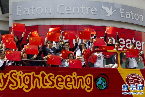 中国侨网9月16日，在加拿大多伦多邓达斯广场，演唱会参与者在停靠于路边的一辆观光车上手持五星红旗演唱并合影。（新华社/邹峥 摄）