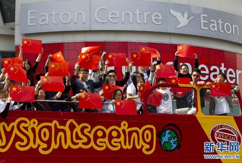 中国侨网9月16日,在加拿大多伦多邓达斯广场,演唱会参与者在停靠于路边的一辆观光车上手持五星红旗演唱并合影。(新华社/邹峥 摄)