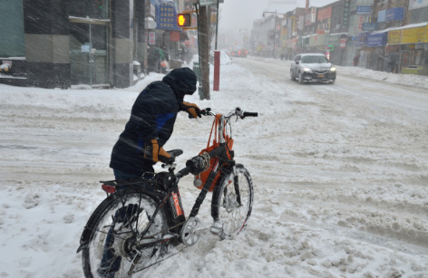 外卖郎在暴雪天连自行车都无法骑，只好牵着车送餐。(美国《世界日报》/朱泽人