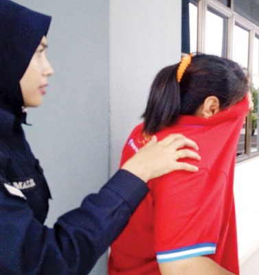 女被告拉高T恤遮盖脸孔。（马来西亚《光华日报》）
