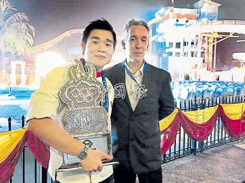 中国侨网拥抱着2017年第3届奥林匹克国际青年厨师大赛亚军奖杯的欧开宾(左),与大会评判合影。(马来西亚《中国报》)