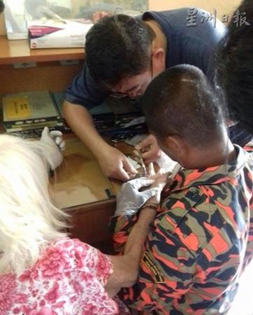 中国侨网消拯官员正在仔细地为华裔年长妇女剪戒指。(马来西亚《星洲日报》)