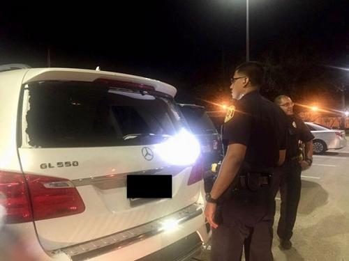 中国侨网糖城警局警员在受害华女被打碎后车窗的奔驰SUV旁展开调查。(陈女士提供图片)