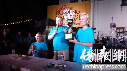 中国侨网黄恩恩(右)巾帼不让须眉,1分钟吃了22个饺子,击败男性PK对手,获得吃饺子大赛的冠军,她捧着奖杯,眼眶湿润。(侨报记者高睿摄)