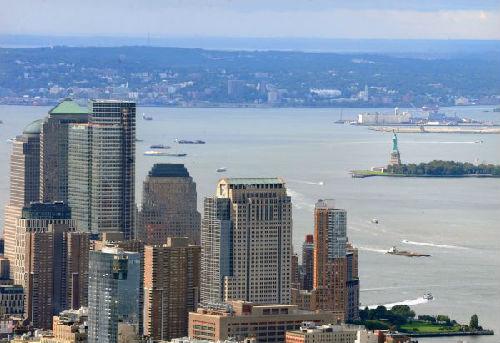 中国侨网资料图：美国纽约曼哈顿下城金融区一带的高楼与自由女神像隔河呼应。（新华社）