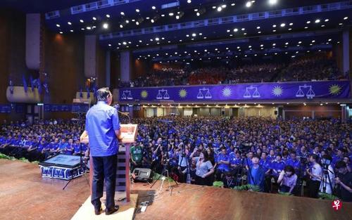 中国侨网廖中莱(背对镜头者)在吉隆坡马华公会大厦礼堂台上宣布其大选竞选宣言。马华党员在台下集体穿上蓝色的国阵党服,全场被一片蓝海淹没,展现团结精神。(新加坡《联合早报》/林国明 摄)