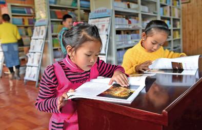 中国侨网两名银井小学的缅甸小学生在瑞丽市姐相乡银井“一寨两国”国门书社里看缅文杂志(2015年1月15日摄)。新华社记者蔺以光摄