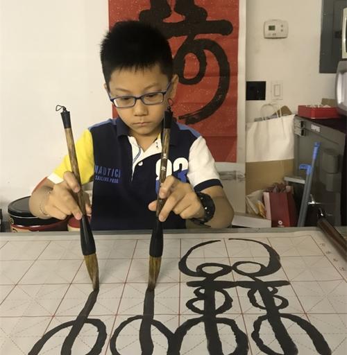 中国侨网于昊辰小小年纪喜爱双手书法,以此了解和学习中国文化。(美国《世界日报》/刘大琪 摄)