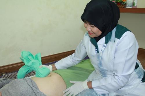中国侨网马来西亚按摩师诺哈雅蒂示范在产妇的腹部进行热敷按摩。（马来西亚《星洲日报》图片）