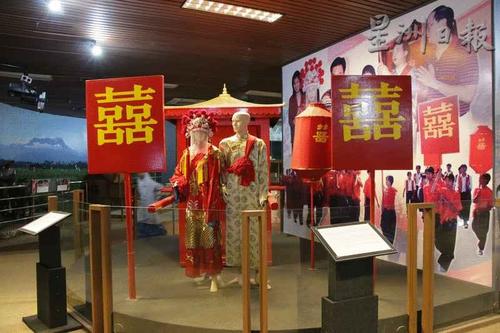 中国侨网文化厅展出华人传统婚礼模型似是而非,解说版上说明新人身穿红色喜衣,但新郎却穿米黄色衣服,背景图案也稍感格格不入。(马来西亚《星洲日报》)