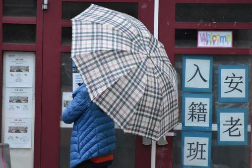 中国侨网日前，叶女士冒雨撑伞等待警岗开门。（美国《世界日报》/李秀兰 摄）