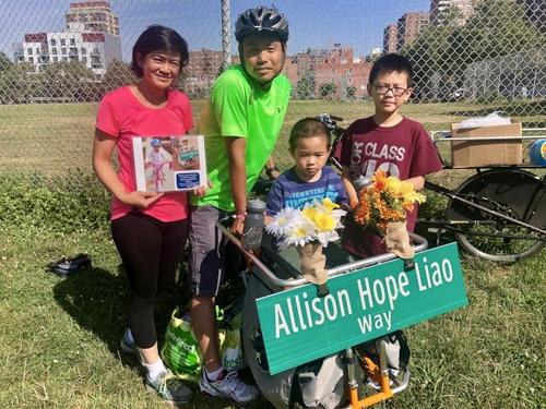 中国侨网廖怡君的父母和兄弟带着廖怡君骑车的照片，以及“廖怡君希望之路”路牌参加骑行活动。(美国《世界日报》/朱蕾 摄)