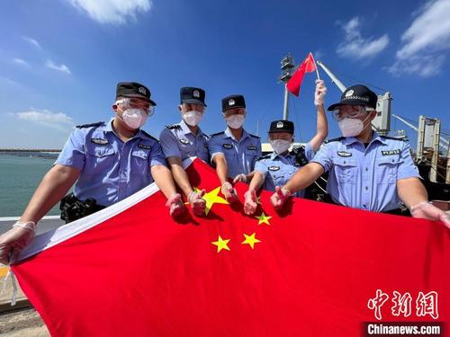 中国侨网在福建莆田秀屿港6号泊位,莆田边检站执勤二队人员在执勤间隙与国旗合影。 唐骏敏 摄