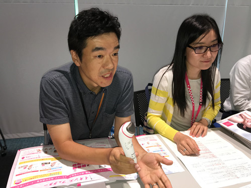 某品牌公司的人员在讲述新款离子美容仪的开发秘话和使用方法。（日本新华侨报网）